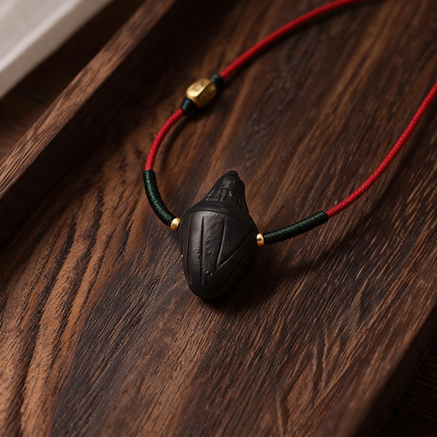 Black Nyangla clay tsatsa pendant with red and green cord flat lay