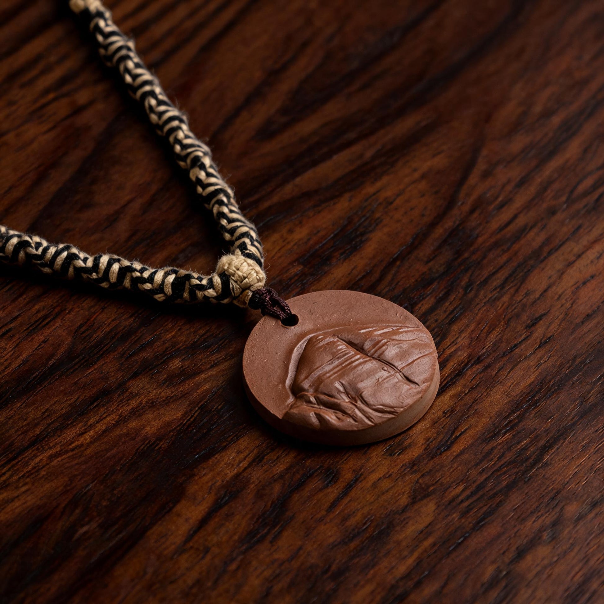 Angled side view of brown clay tsatsa pendant