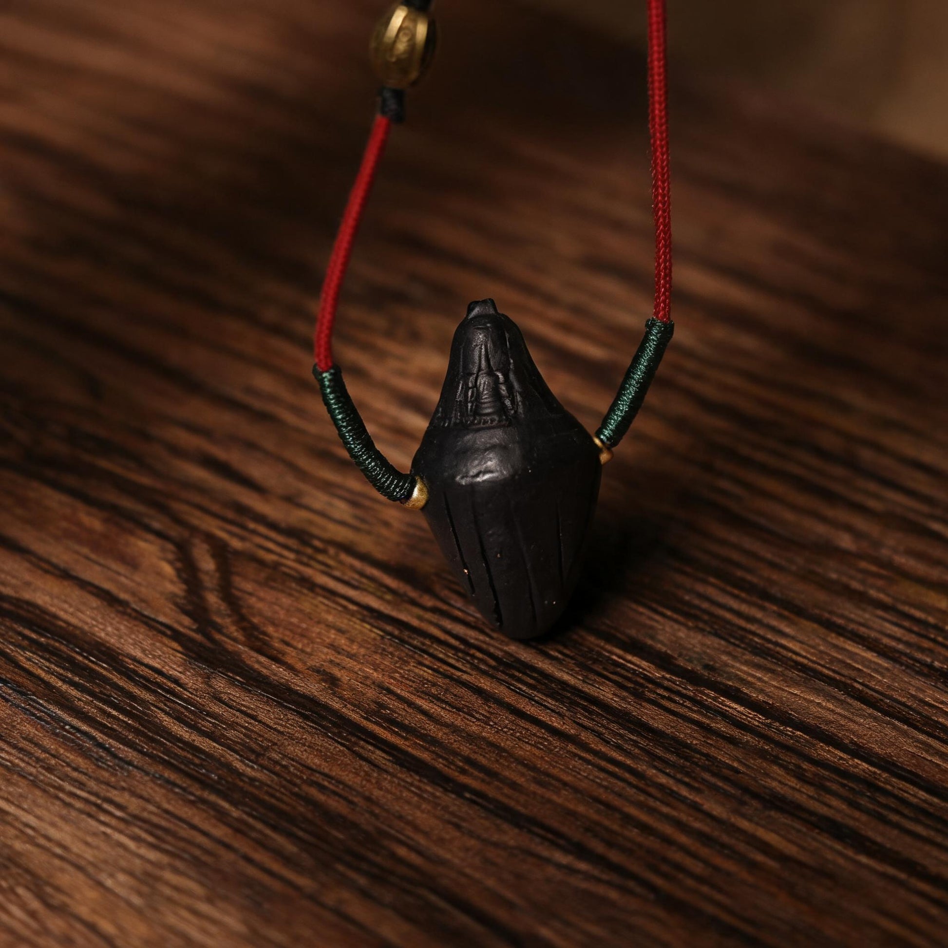 Angled side view of black pointed Nyangla clay tsatsa pendant
